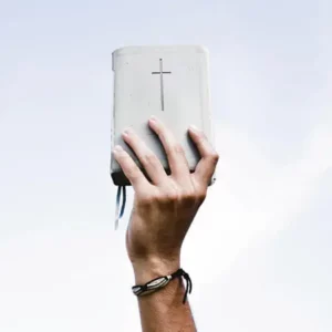 Ein Buch mit einem Kreuz wird von einer Hand hochgehalten
