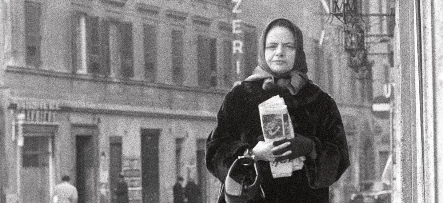 Elsa Morante mit Zeitung in der Hand auf einer Straße.