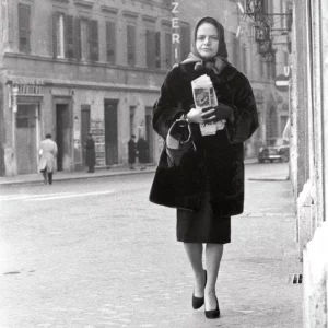 Elsa Morante mit Zeitung in der Hand auf einer Straße.