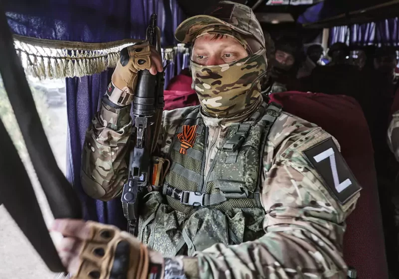 Ein vermummter, russischer Soldat mit Gewehr in einem Bus.