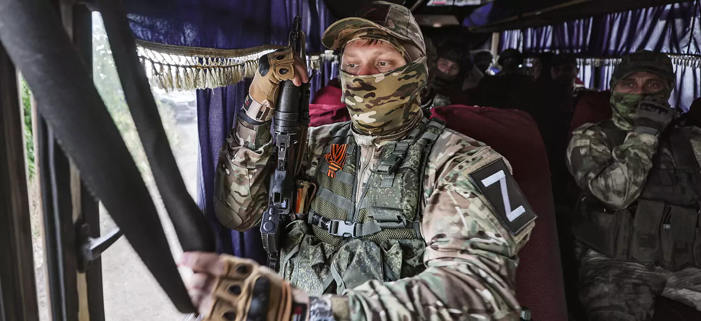 Ein vermummter, russischer Soldat mit Gewehr in einem Bus.