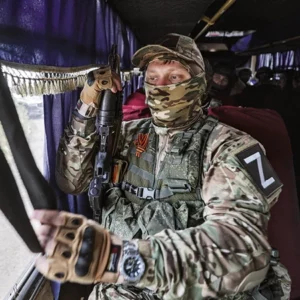 Ein vermummter, russischer Soldat mit Gewehr in einem Bus.