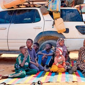 Familie mit Hab und Gut vor einem Auto sitzend